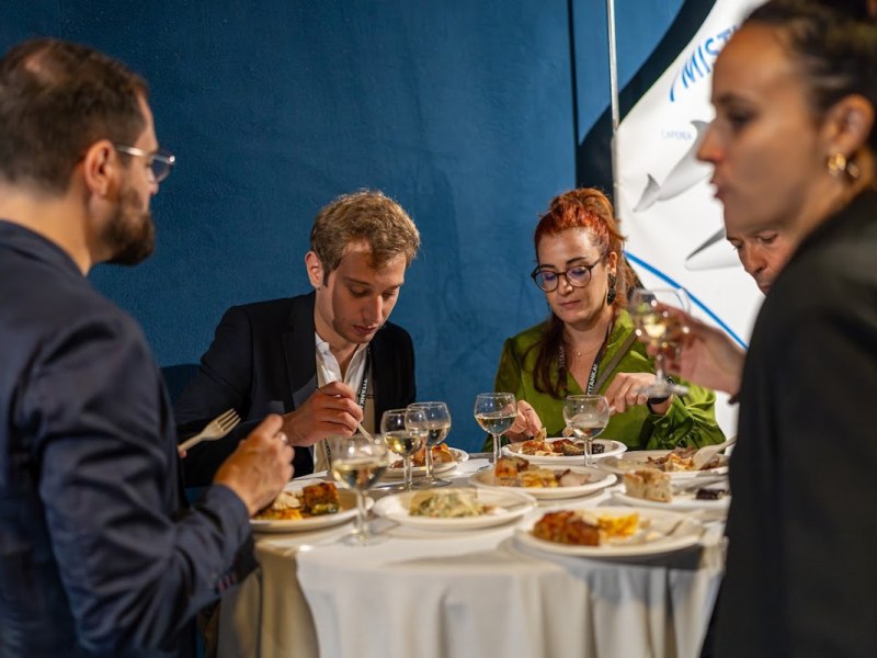 Un gruppo di persone che mangia e beve vino attorno a un tavolo rotondo.