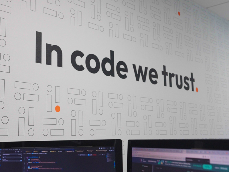 Parete con la scritta 'In code we trust' in un ufficio di programmazione.