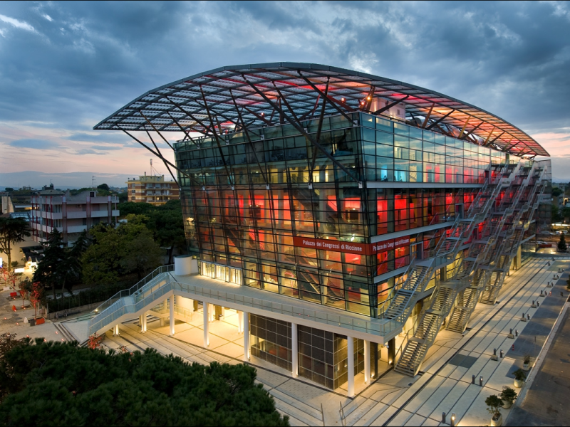 Il moderno Palazzo dei Congressi di Riccione con facciata in vetro e luci rosse.