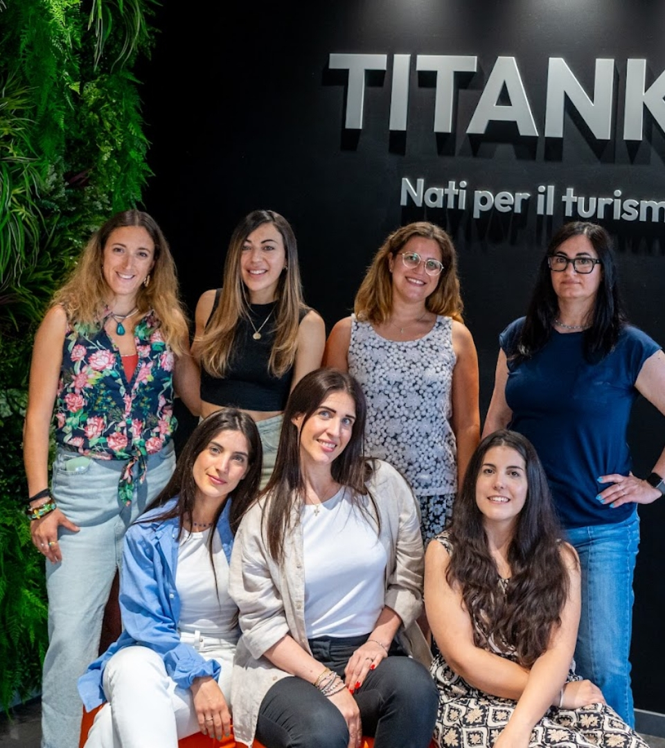 Gruppo di donne sorridenti davanti a un'insegna aziendale con scritta 'TITANKA'.