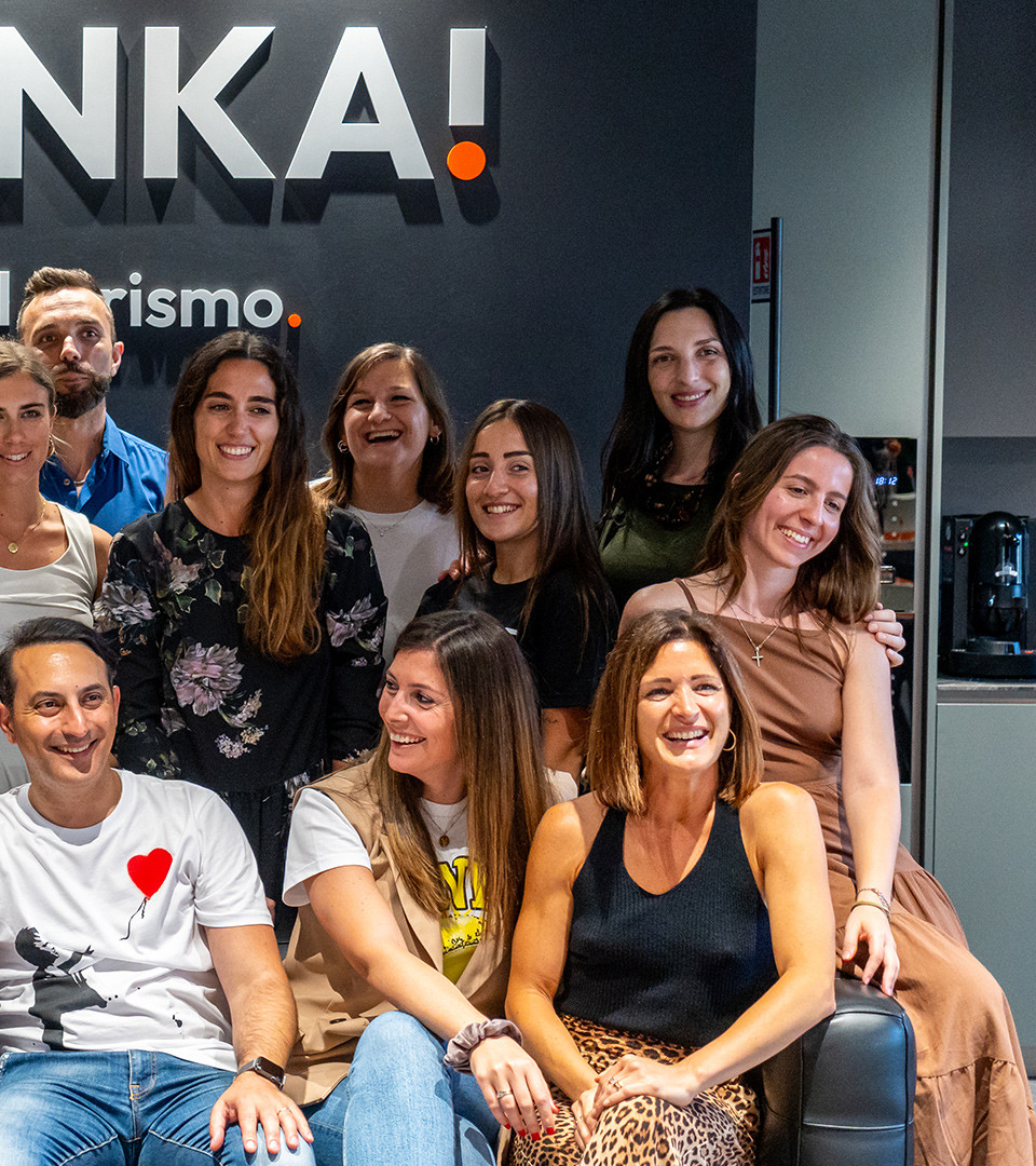 Gruppo di persone sorridenti in ufficio con insegna 'ANKA!' sullo sfondo.