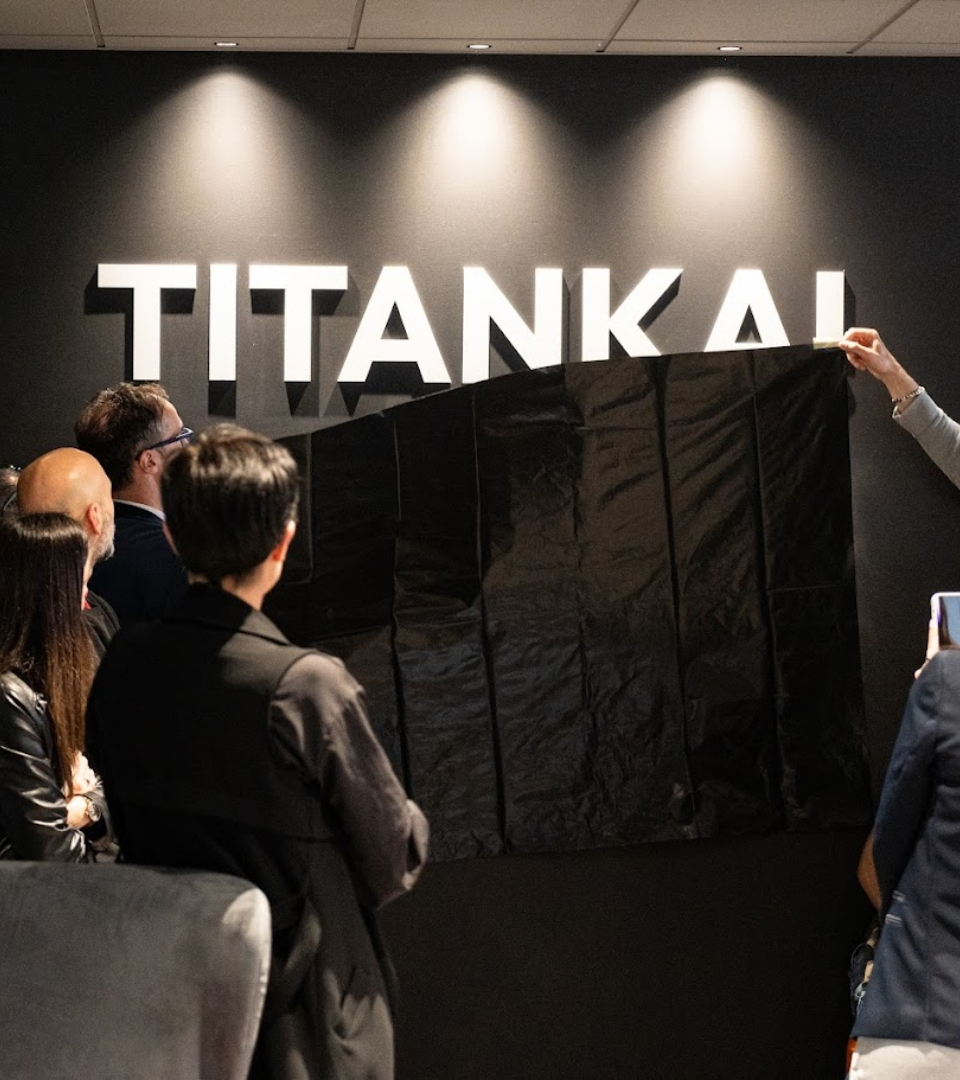 Inaugurazione del logo TITANKAI con pubblico presente e copertura nera parzialmente rimossa.