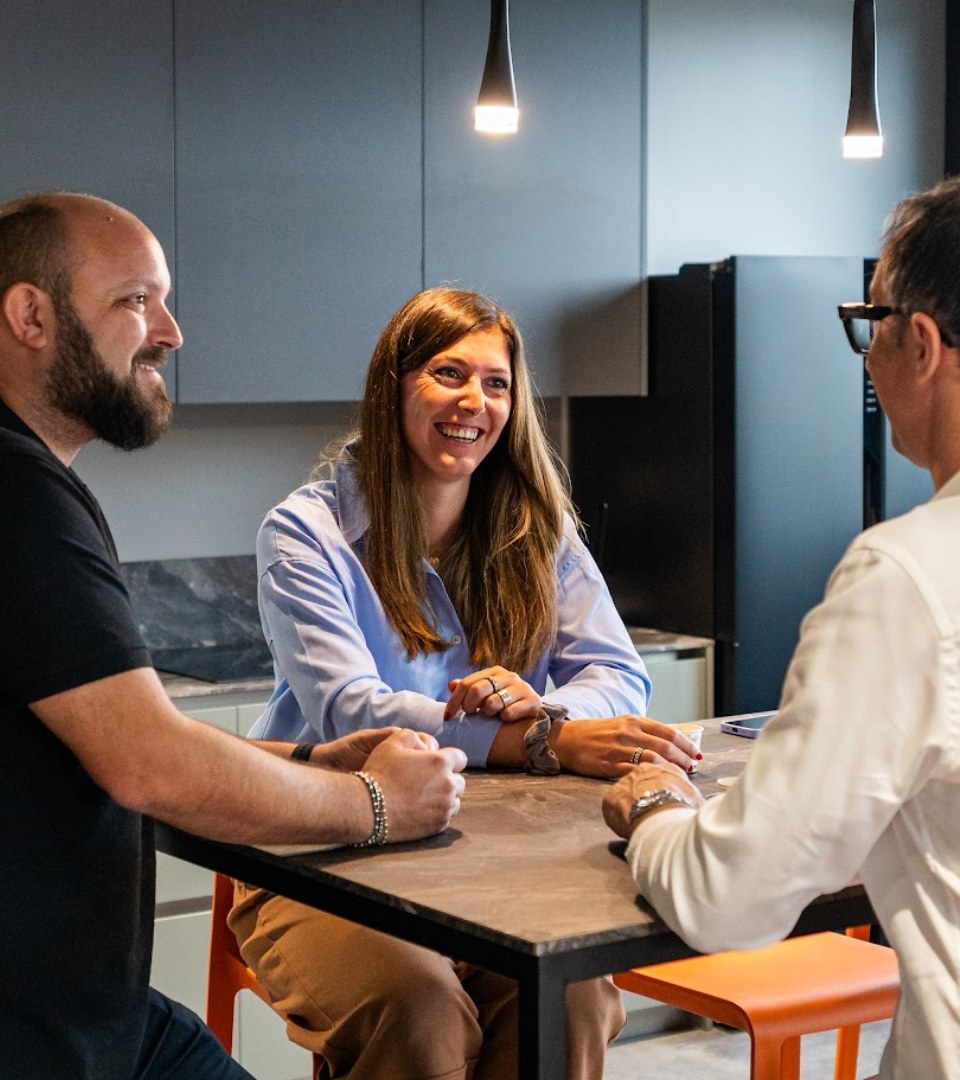 Tre persone conversano attorno a un tavolo in un ambiente moderno e illuminato.